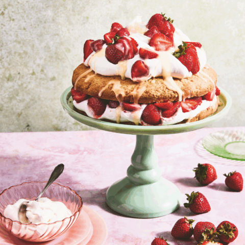 Dolly Parton's strawberry shortcake on a mint green cake pedestal, surrounded by strawberries and a bowl of whipped cream.