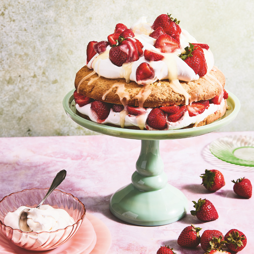 Dolly Parton's strawberry shortcake on a mint green cake pedestal, surrounded by strawberries and a bowl of whipped cream.