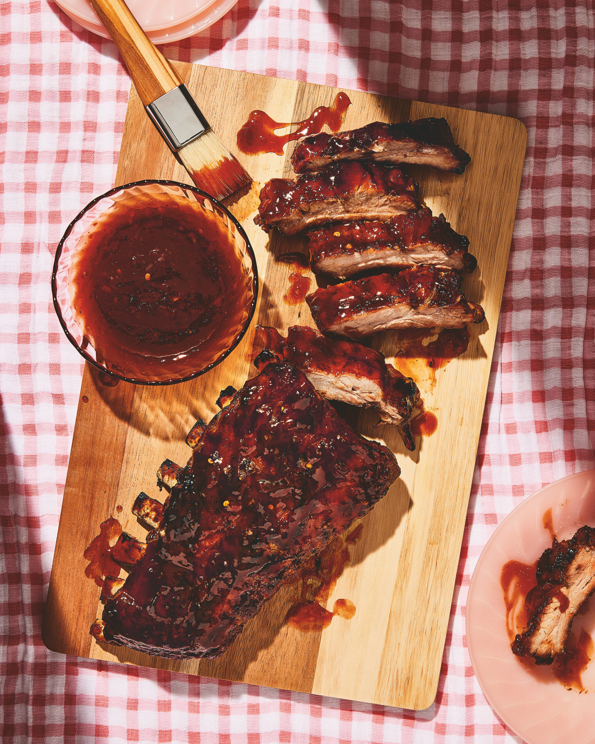Best Barbecue Ribs Recipe from Dolly Parton with barbecue sauce on the side. Ribs aresitting on a wooden board