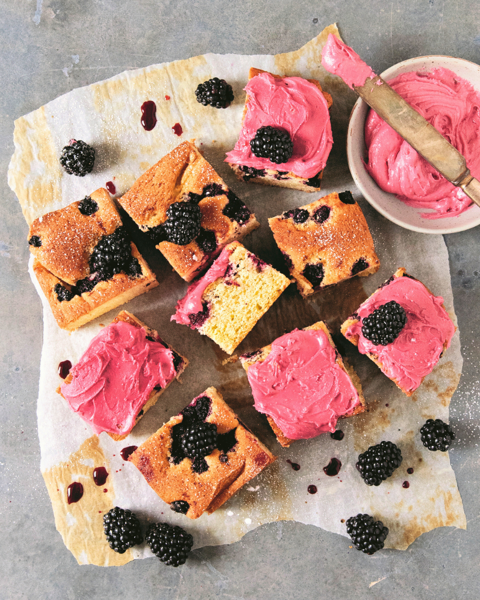 Overhead shot of Blackberry Almond Snacking cake recipe cut into squares with pink frosting.