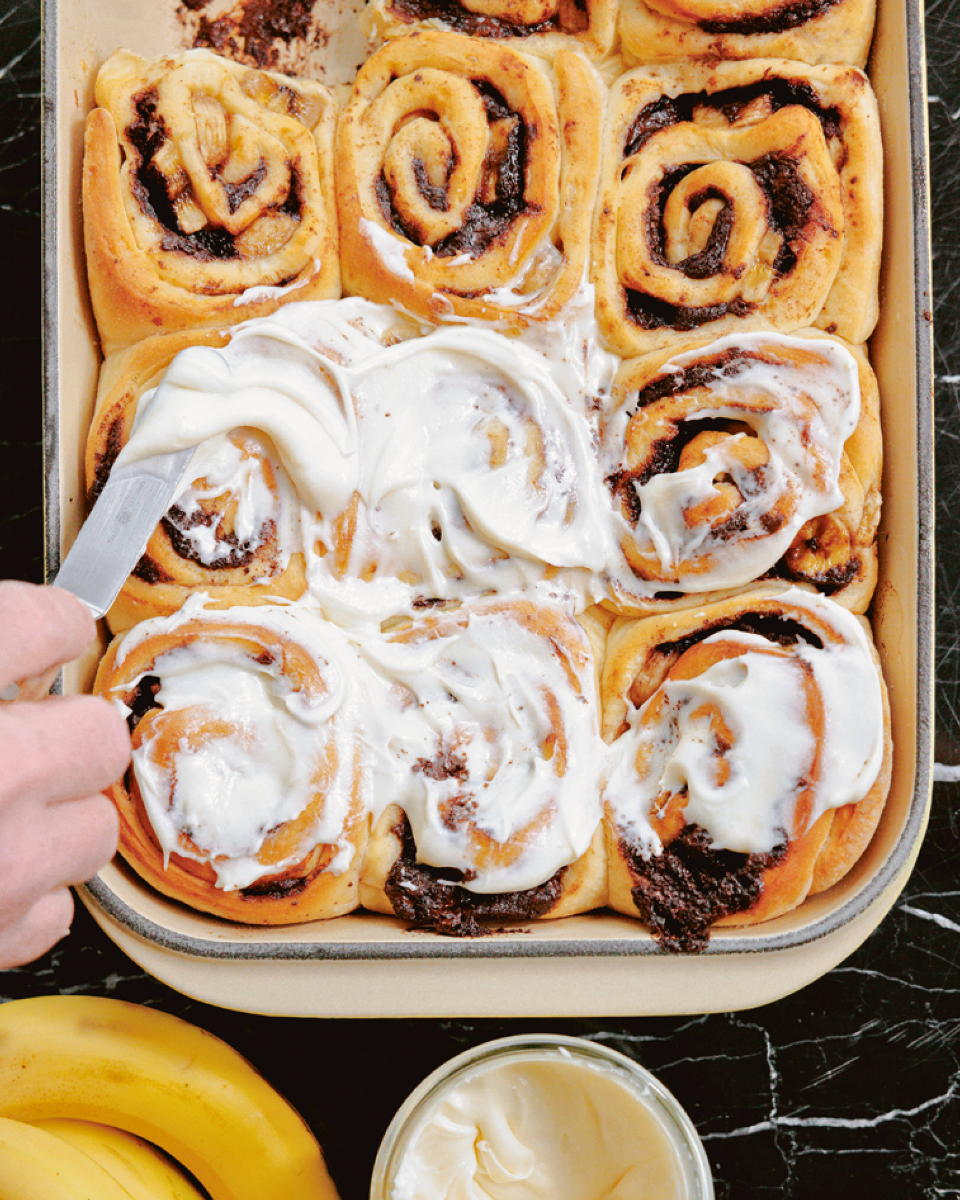 Cream cheese frosting is spread overtop a spread on top of chocolate banana swiirod