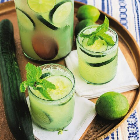 One pitcher and two glasses filled with cucumber lime agua fresca on a brown platter.