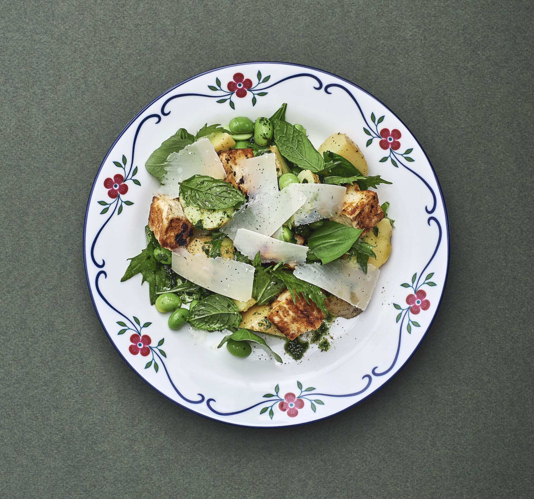 White plate with red decorative flowers on the edge topped with potato salad and halloumi.