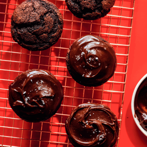 Four mini chocolate fudge cakes on a wire rack with a red background.