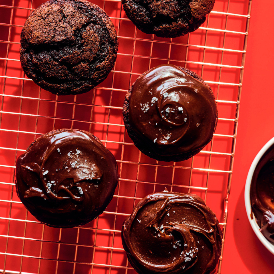 Four mini chocolate fudge cakes on a wire rack with a red background.