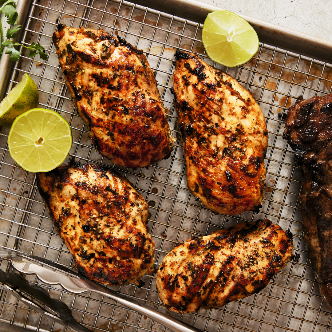 Four grilled chicken breasts on a wire rack with lime halves next to it.