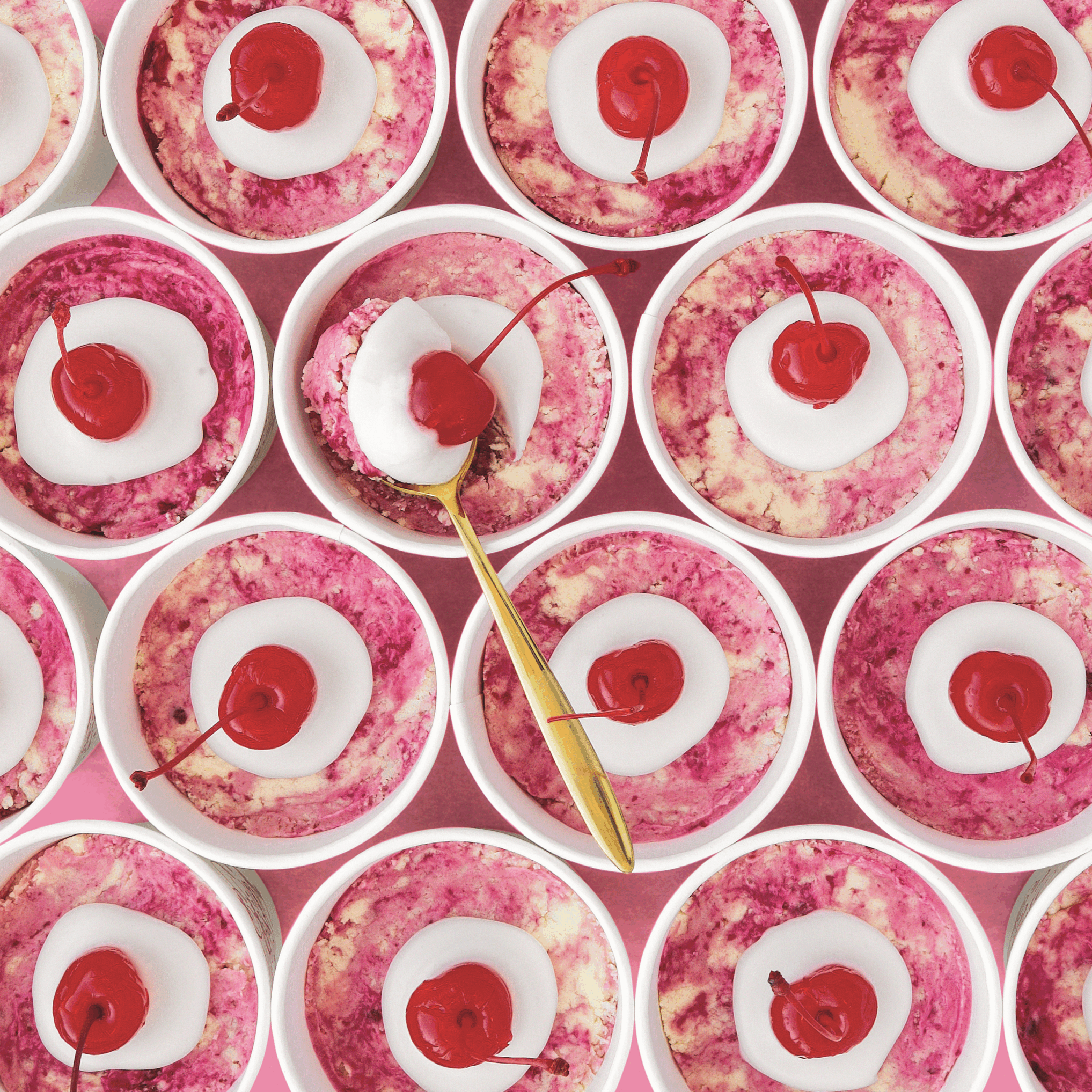 A close-up of pink cookie dough cups topped with a dollop of white icing glaze and maraschino cherries.