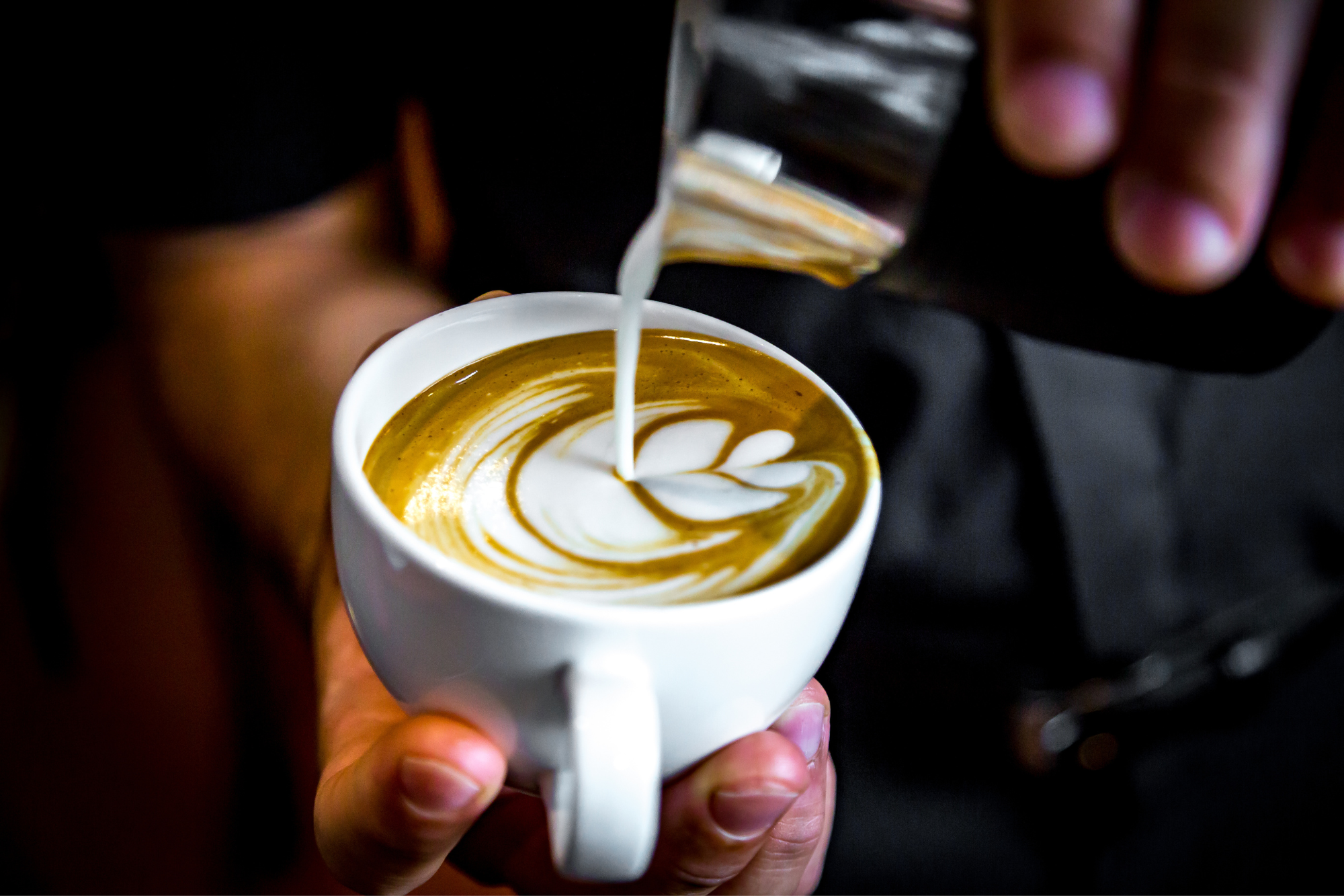 Coffee cup with steamed milk being poured slowly into it