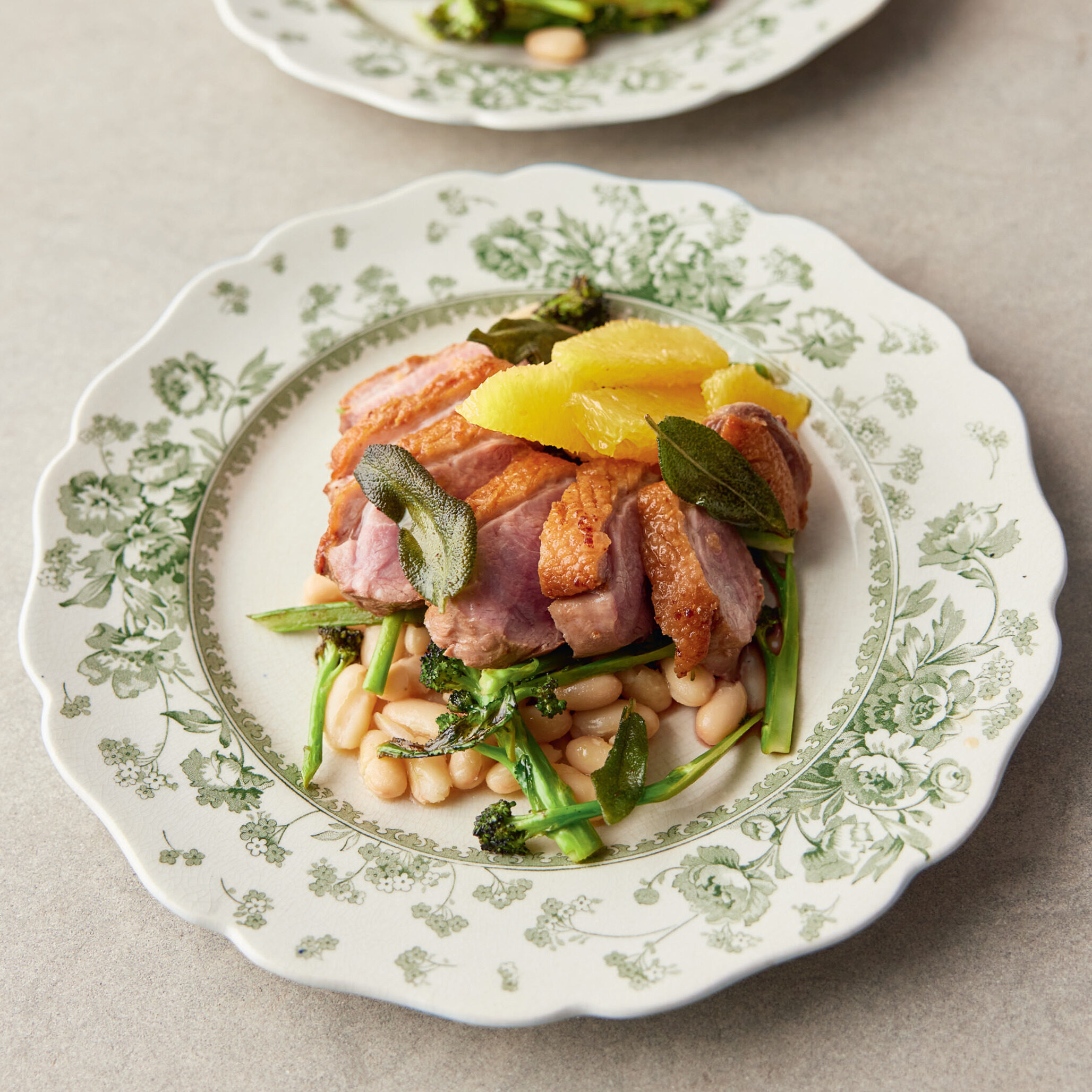 White plate topped with crispy duck, creamy white beans and charred broccolini.