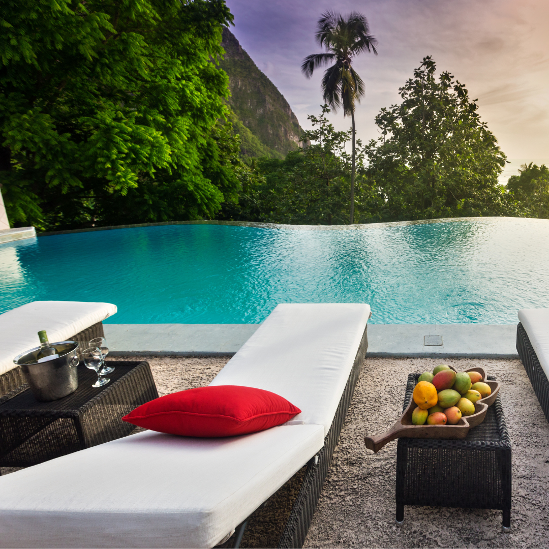 White lawn chairs topped with a red pillow overlooking a pool, with mountains and trees in the background.