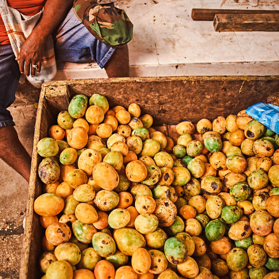 A large wooden box filled with orange and green Colombian sugar mangoes.
