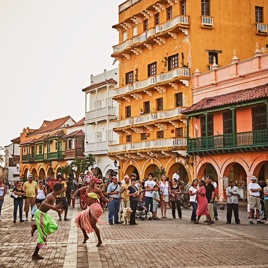 A crowd watches two dancers in the streets with colourful colonial-style buildings in the background.