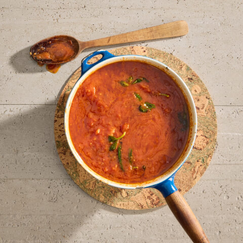 A pot full of tomato sauce with basil leaves on a circular cork pad.