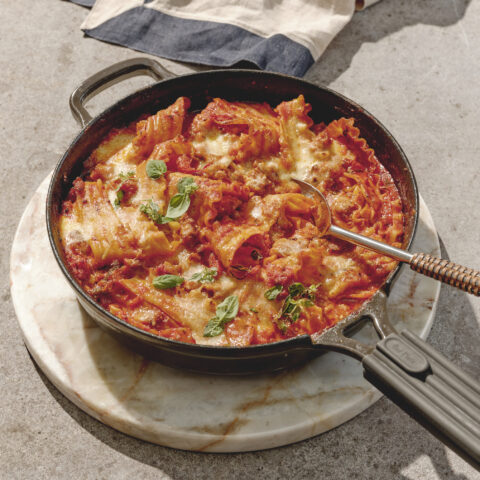 A skillet with broken lasagna pieces in a red sauce with cheese and basil.