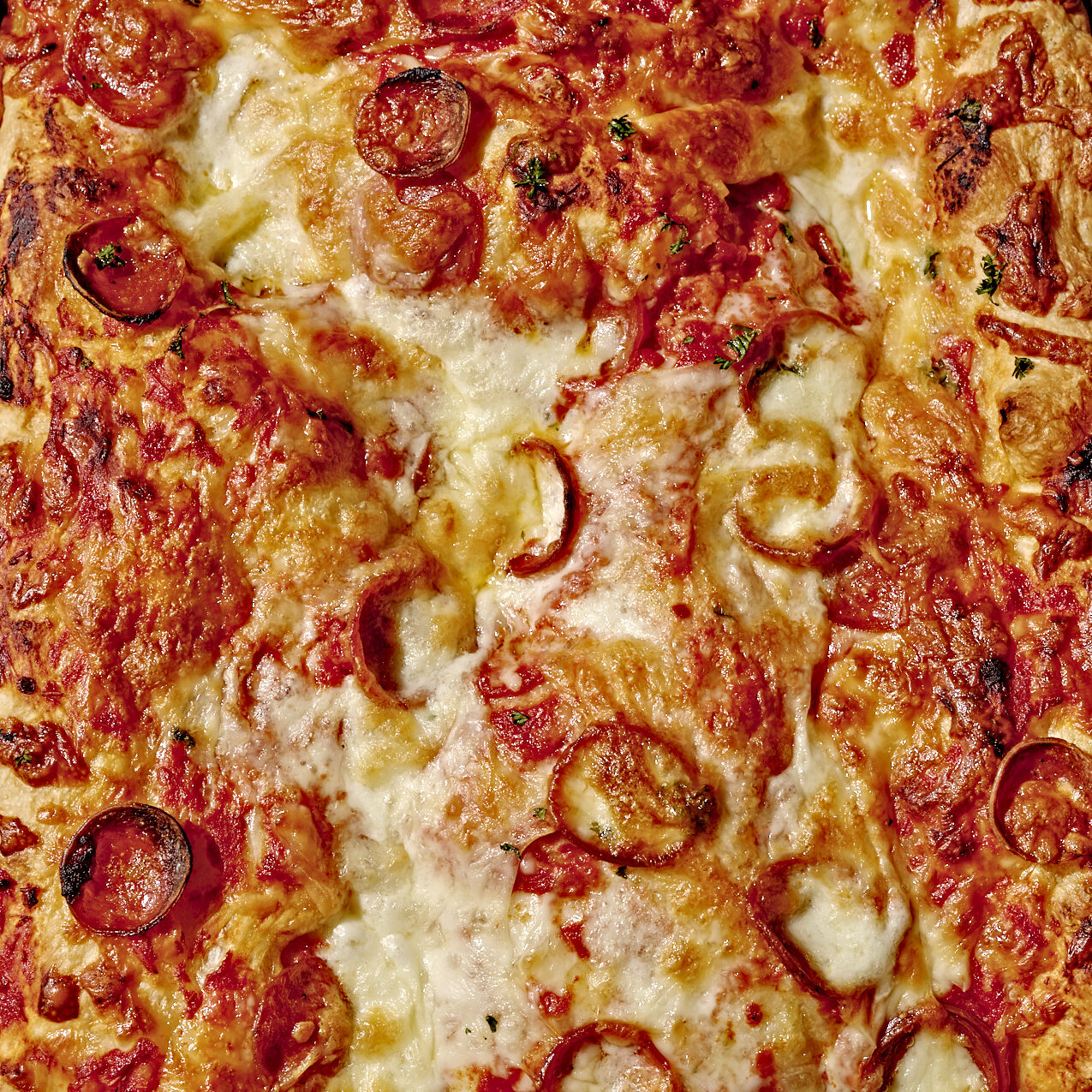 Focaccia bread pizza with pepperoni slices and cheese in a metal baking pan.