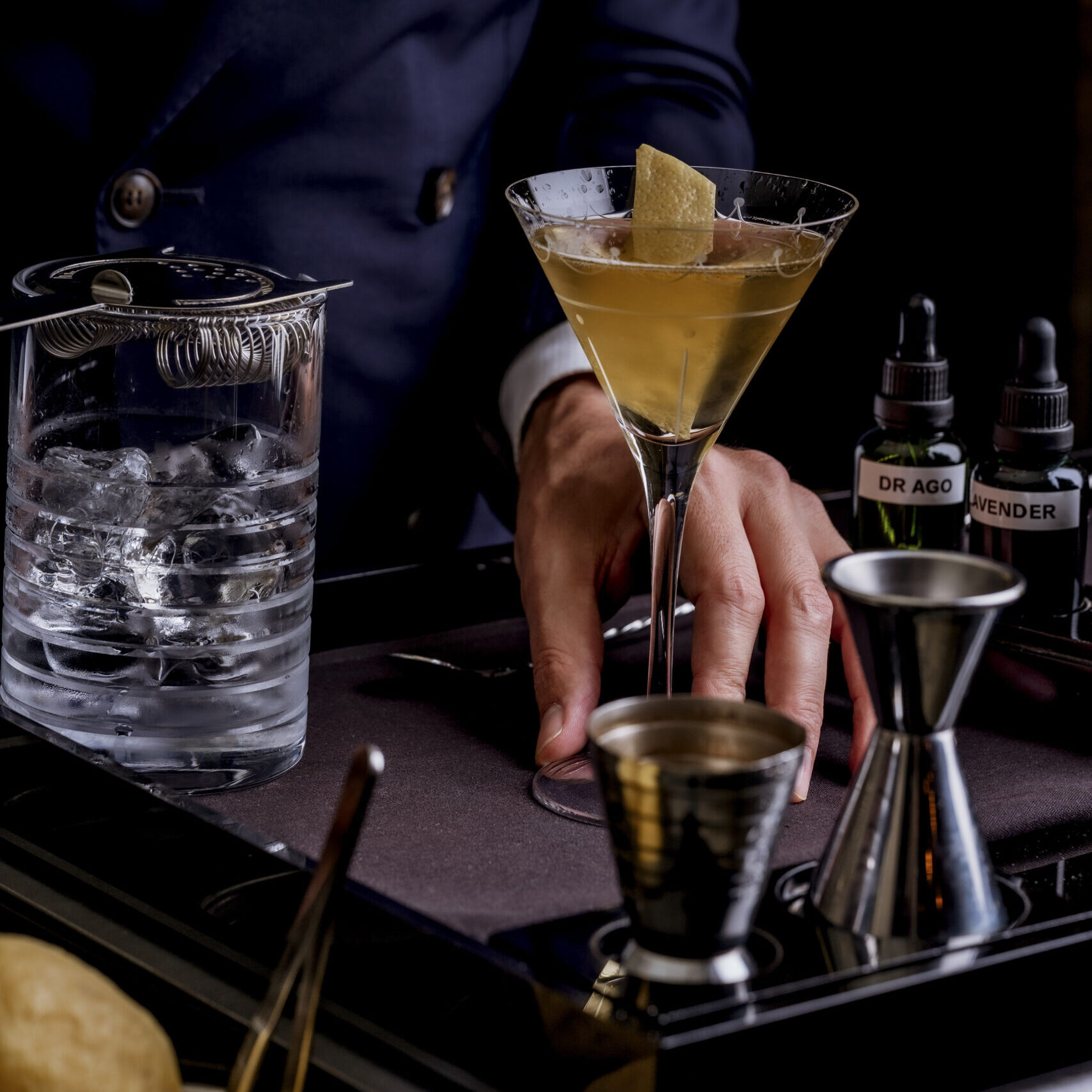 A hand holding a martini glass garnished with lemon peel.