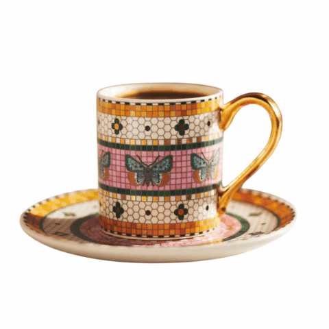 An espresso cup with gold details and a butterfly mosaic pattern on a matching saucer.