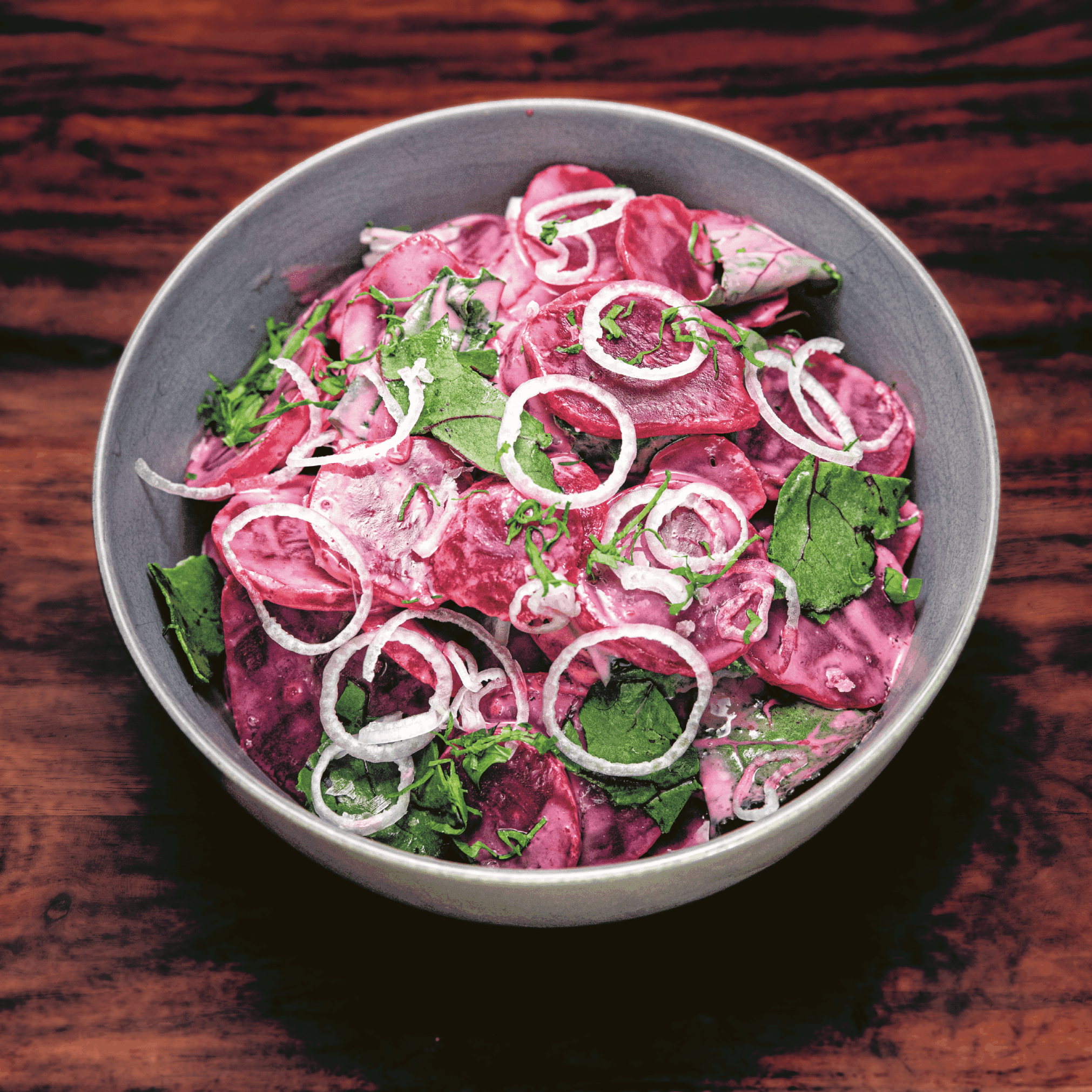 A gray bowl of beets with red onion.