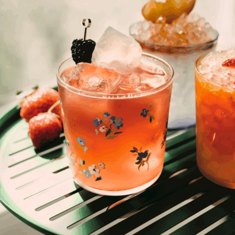 A clear glass filled with ice, red liquid and a blackberry on a skewer.
