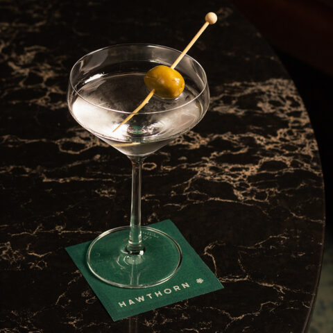 A martini glass garnished with a skewered olive, on a square green coaster.