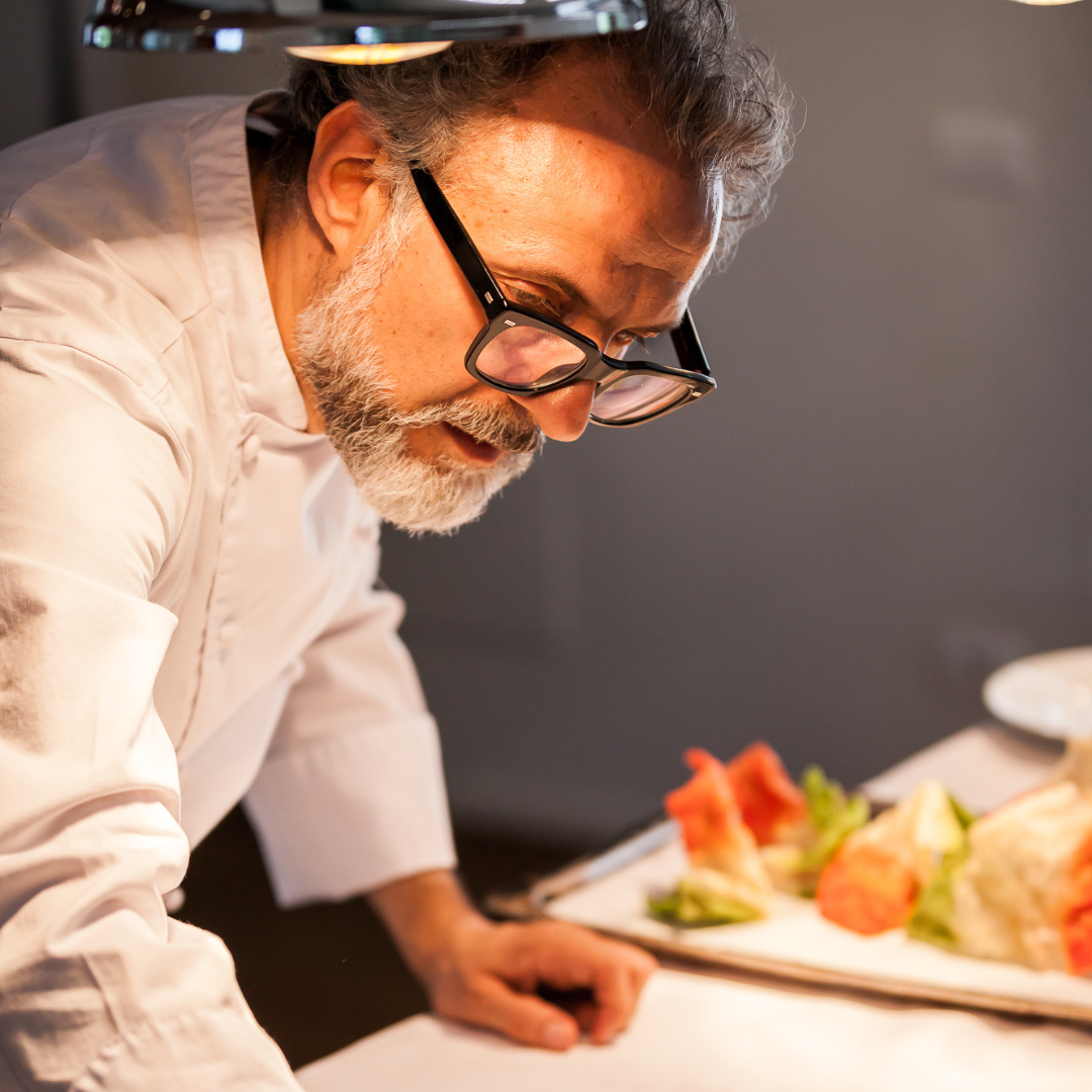 Man with white beard and glasses in a chef's coat in the kitchen.