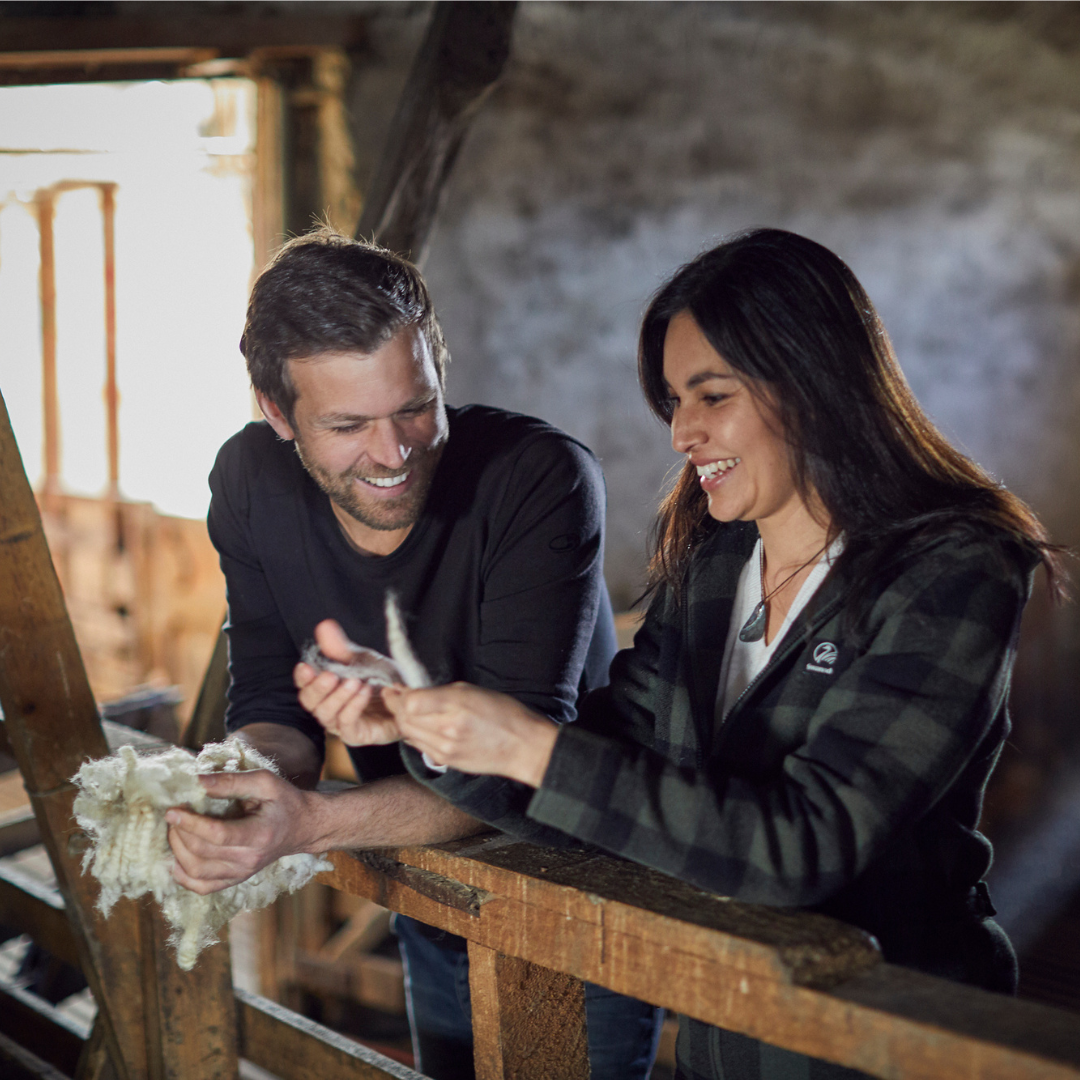A man and a woman holding wool inside a barnyard. 