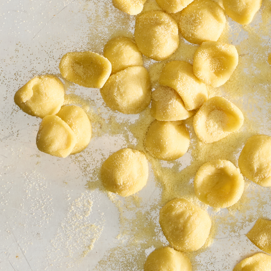 Pieces of uncooked orecchiette pasta on a reflective surface.