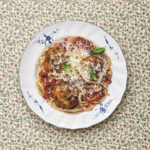 A plate with spaghetti, tomato sauce, grated parmesan and basil.