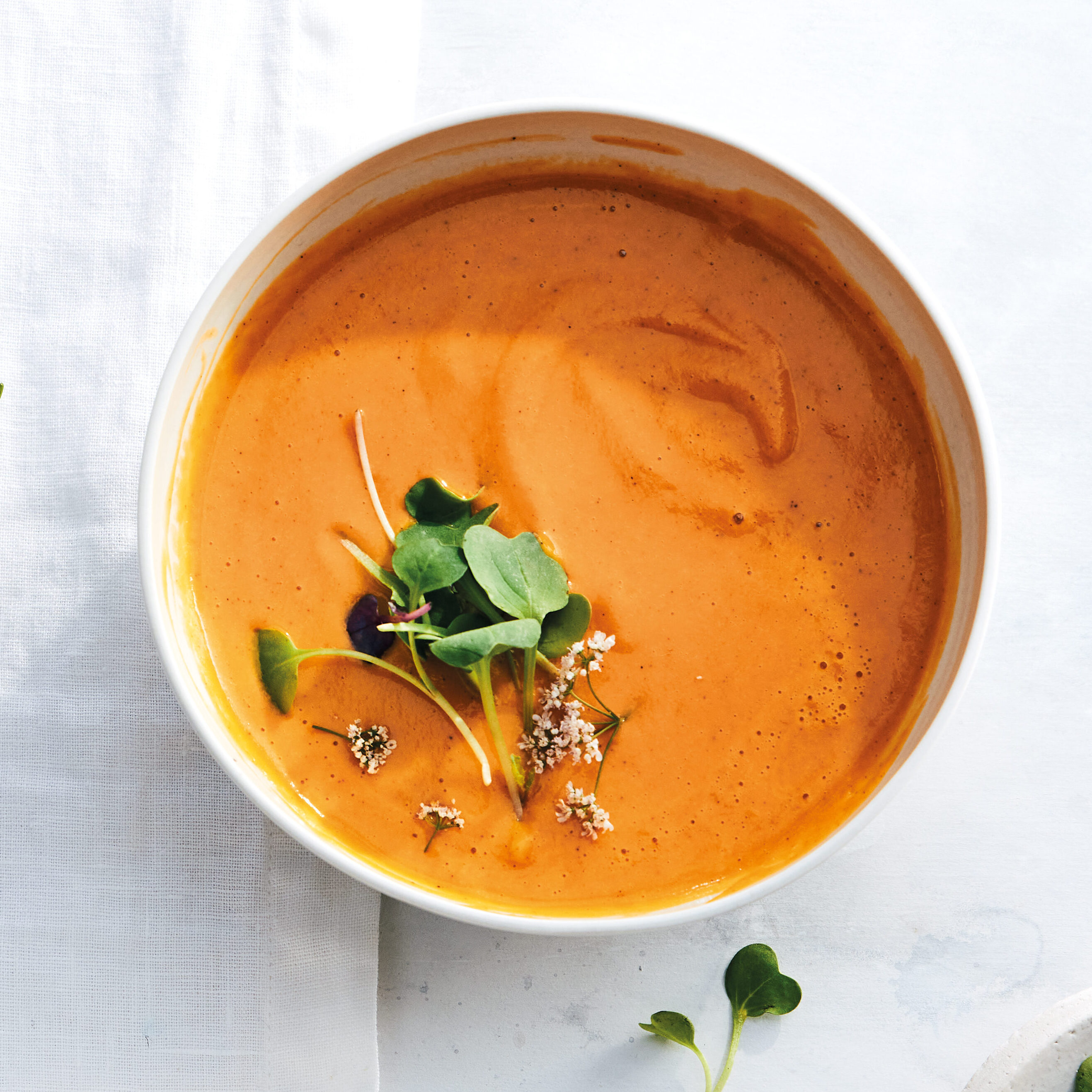 A bowl of creamy carrot soup topped with some microgreens.