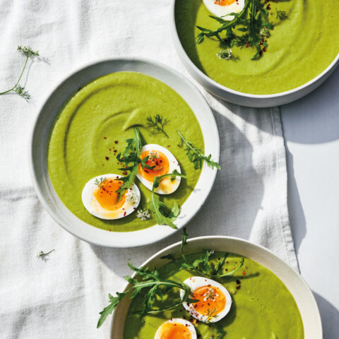 Three bowls of green soup topped with arugula and two halves of a jammy egg.