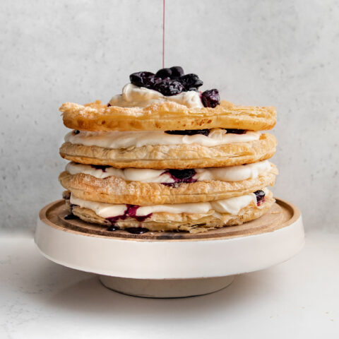 A cake on a white cake stand made from layers of puff pastry, cream and cherry compote.
