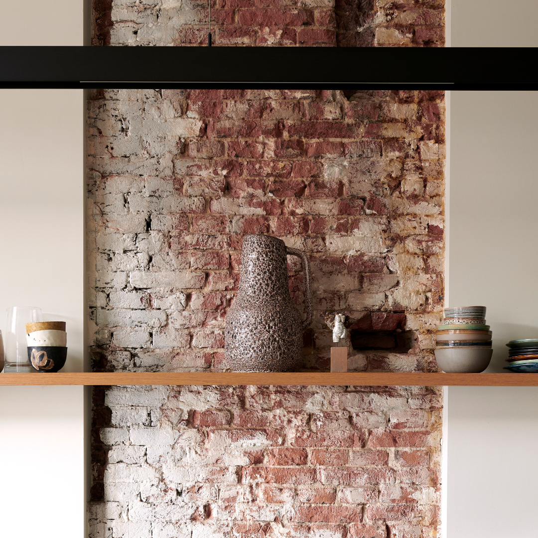 A wooden shelf holding various ceramic pieces in front of an exposed brick wall.