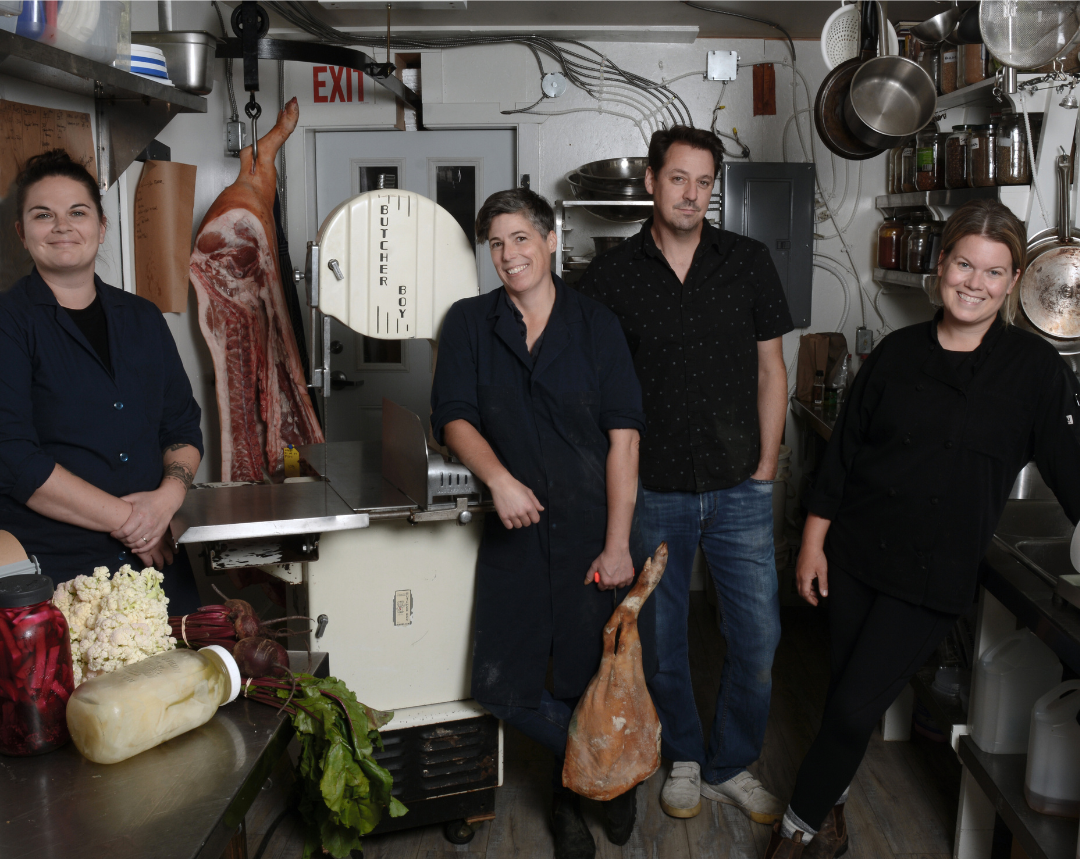 Four people in black t-shirts standing amongst butcher equipment.
