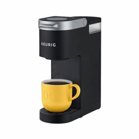A black coffee maker with a yellow mug full of coffee on the base.