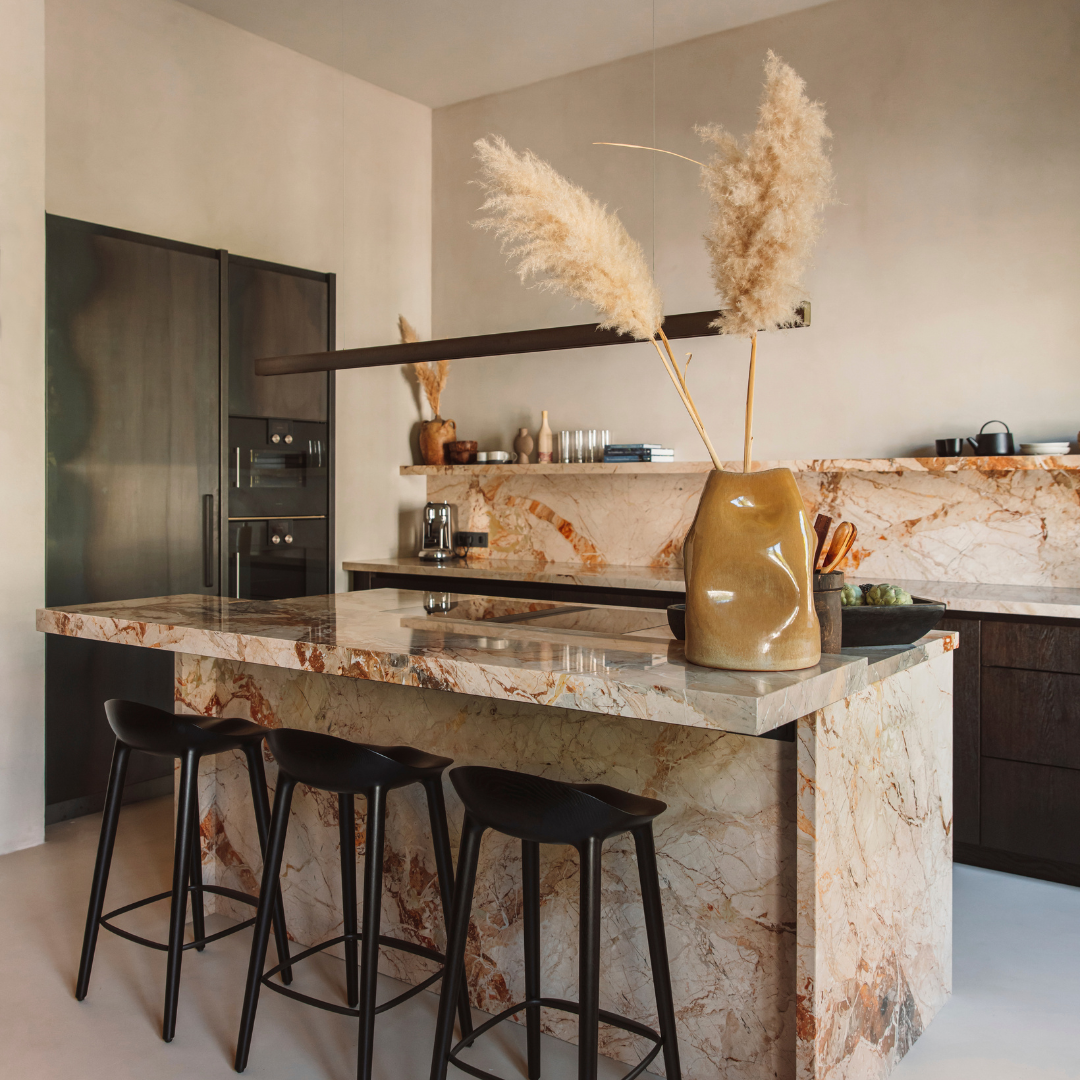 A marble kitchen island with three stools in a tan and brown-coloured kitchen. 