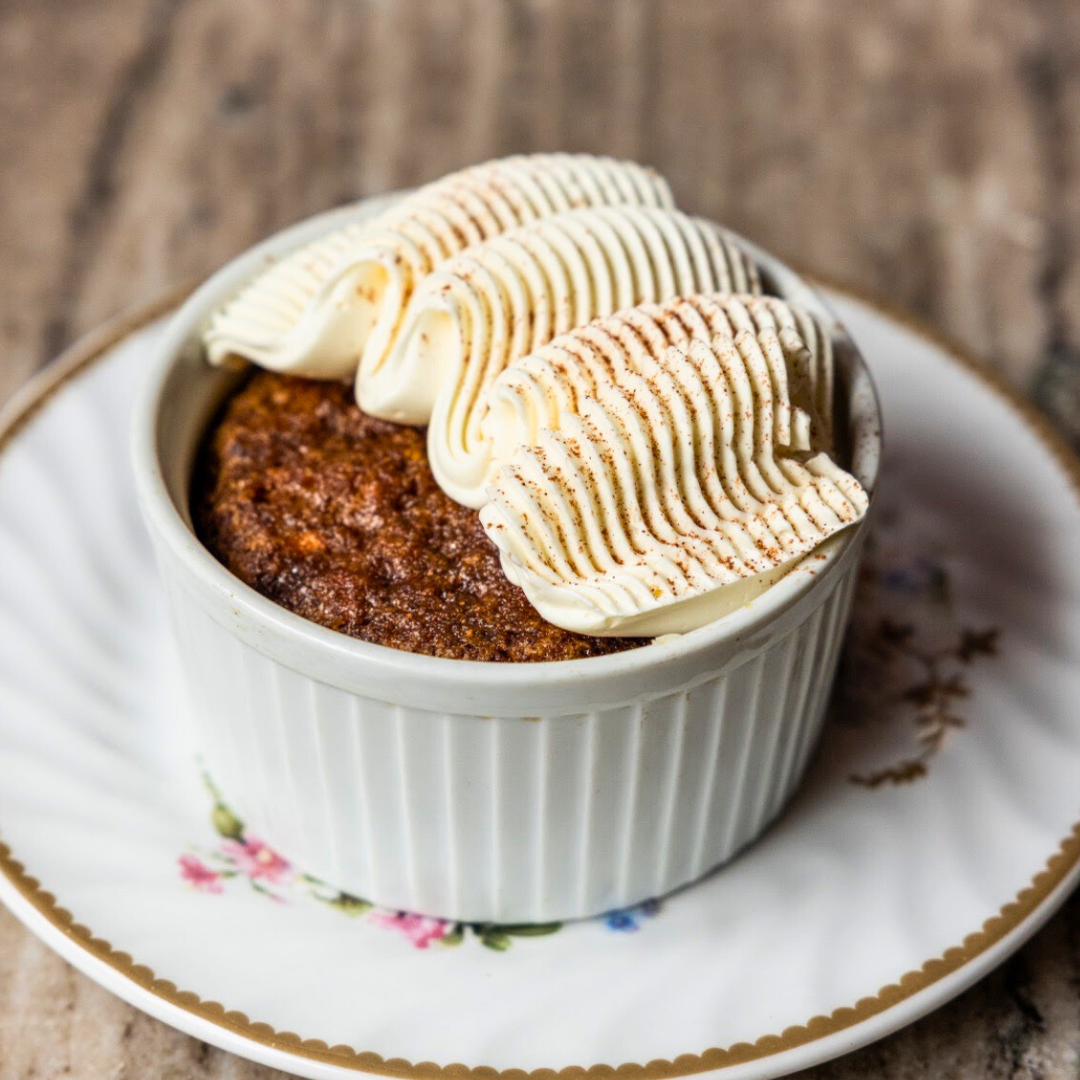 A pumpkin cake topped with piped frosting in ramekin on a floral saucer.