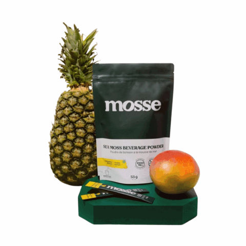 A package labelled "mosse" on a green pedestal besides a pineapple, a mango and two sticks of powder.