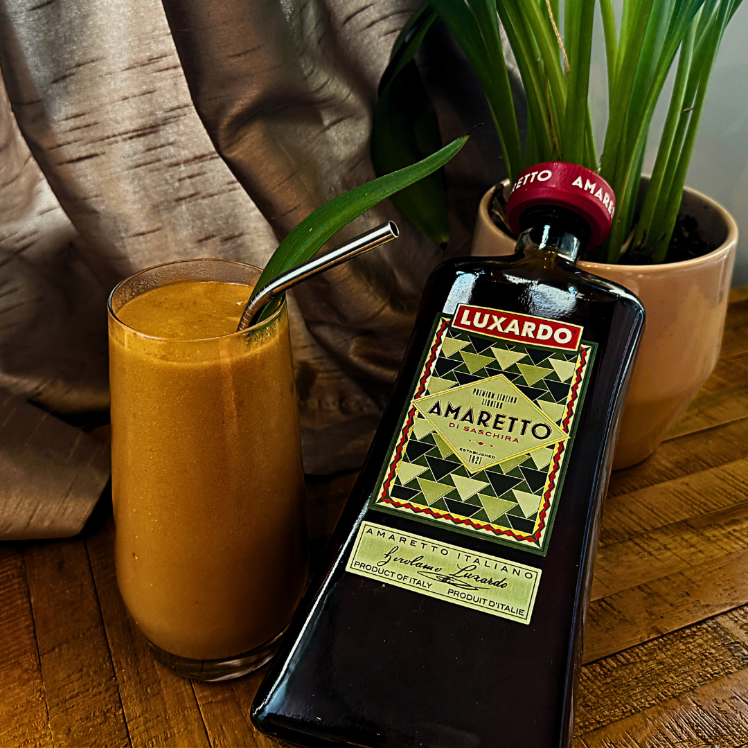 A glass filled with orange liquid and a silver straw next to a bottle of amaretto. 