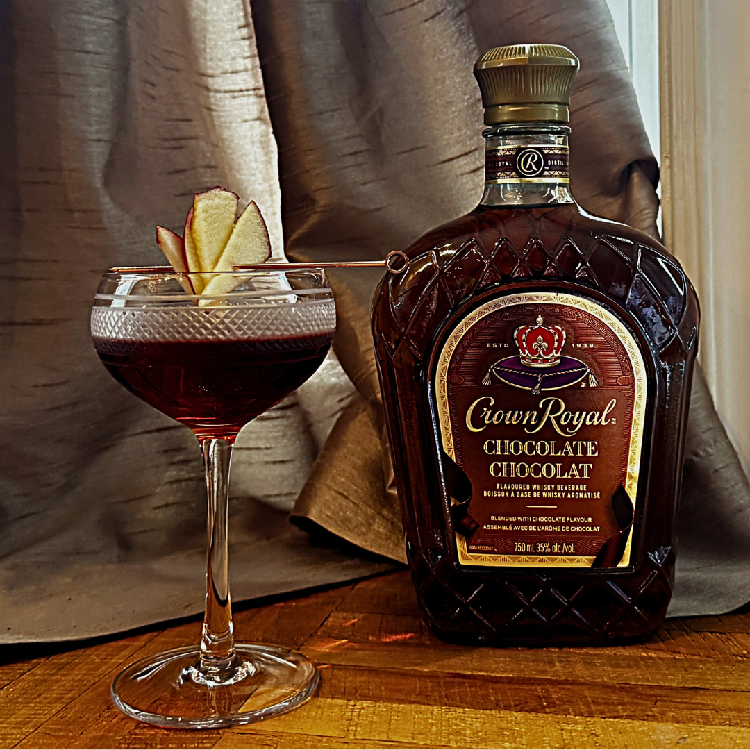 A cocktail glass with garnish next to a bottle of Crown Royal Chocolate. 