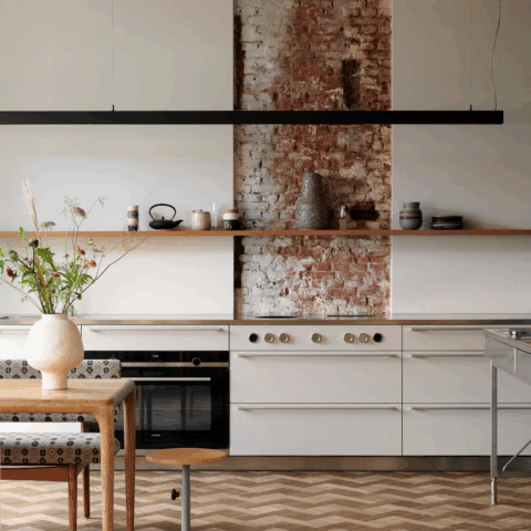 A bright kitchen with a patterned tile floor, a wooden table and white cabinets.
