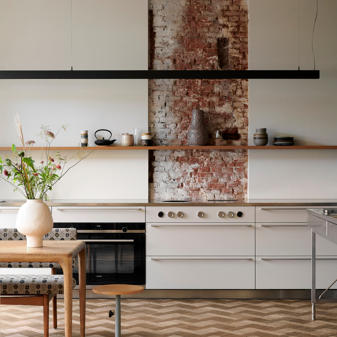 A bright kitchen with a patterned tile floor, a wooden table and white cabinets.