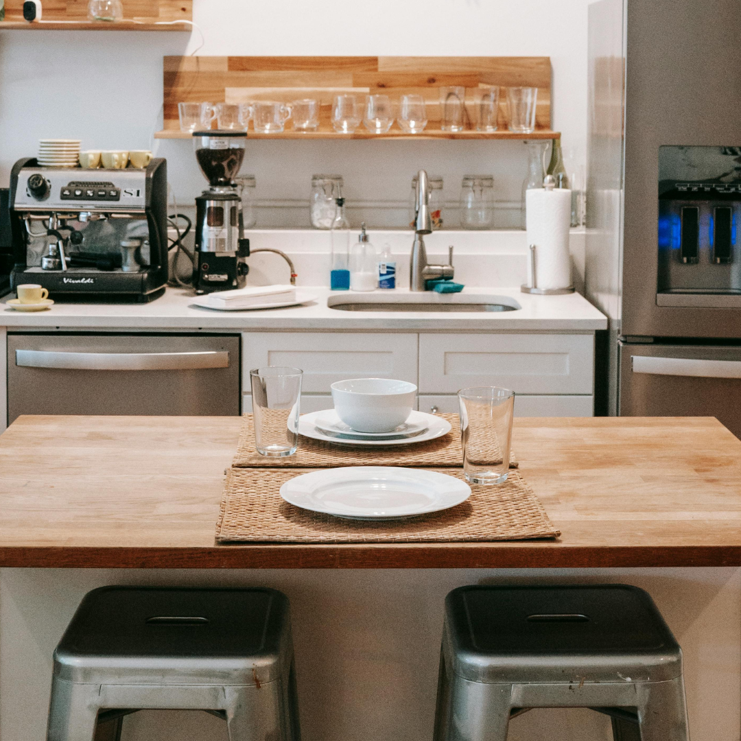 A kitchen island with two silver stools with a counter, fridge and appliances in the background. 