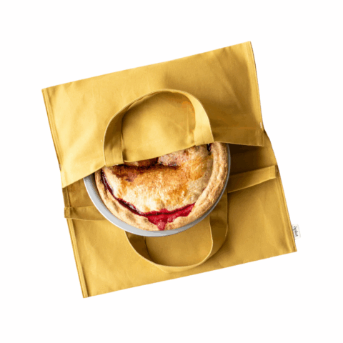 A yellow fabric dish tote with handles opened in the middle to show a baked pie.