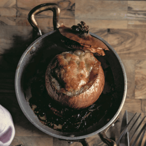 A baked onion in a silver pot on a wooden board.