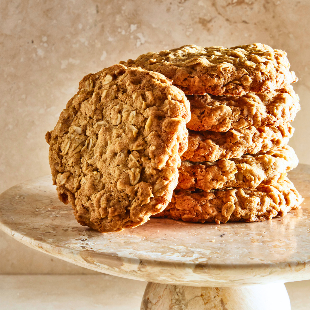 Six oatmeal cookies stacked on top of a marble cake stand on a marble countertop.
