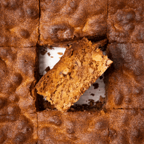 A sliced pan of blondies with the centre square flipped on its side, revealing chopped pecans inside.
