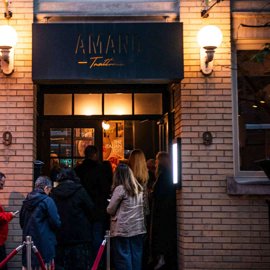 Exterior of amano trattoria at twilight with people lined up for the elle gourmet event