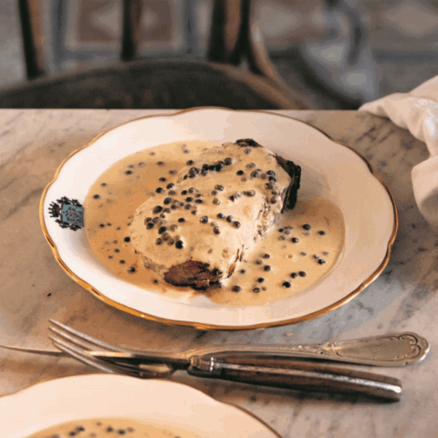 A filet topped with a cream sauce and black peppercorns on a white plate.