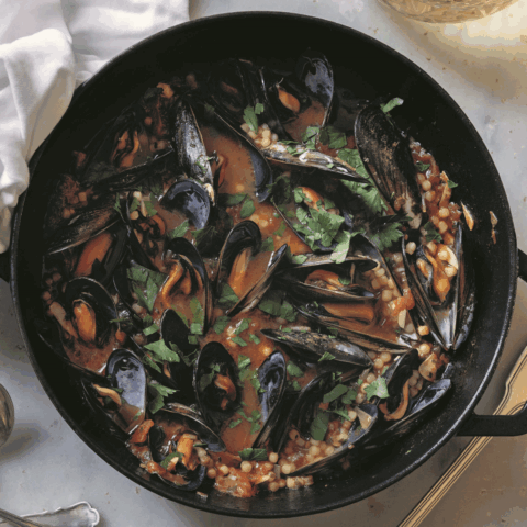 A black pan with mussels in a tomato sauce on a marble table