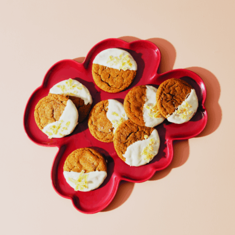 Eight ginger cookies half-dipped in white frosting and garnished with candied ginger on a red plate.